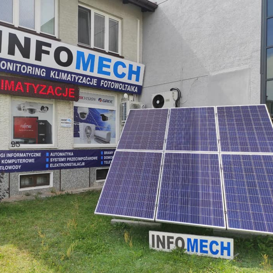 Instalacja paneli fotowoltaicznych przed siedzibą firmy w Stalowej Woli, widoczny szyld z ofertą: monitoring, klimatyzacja, fotowoltaika oraz jednostka zewnętrzna klimatyzatora.