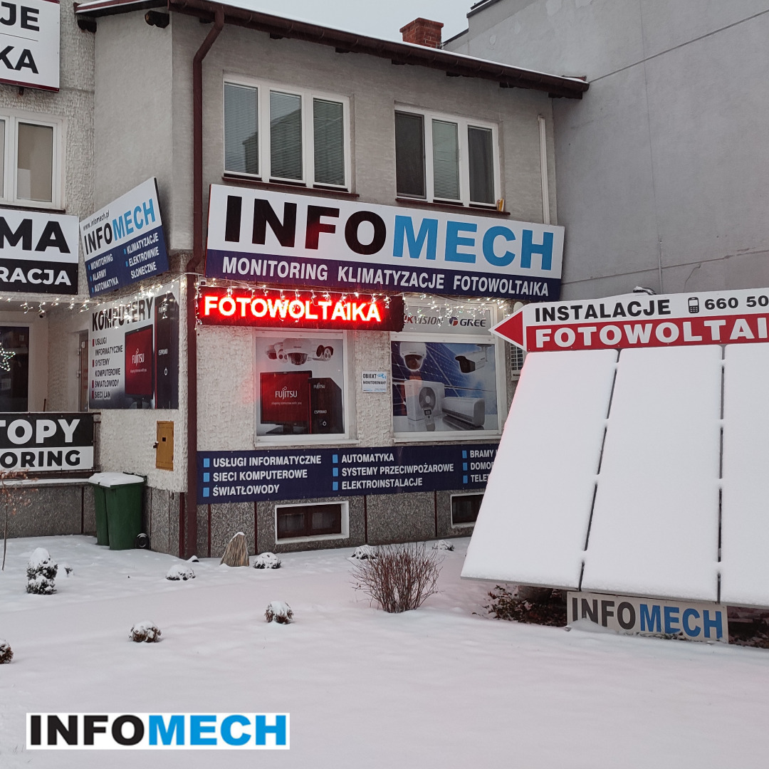 Budynek firmy INFOMECH w zimowej scenerii, oferującej usługi montażu i serwisu instalacji fotowoltaicznych, klimatyzacji i monitoringu, z neonowym napisem 'FOTOWOLTAIKA' nad witryną.