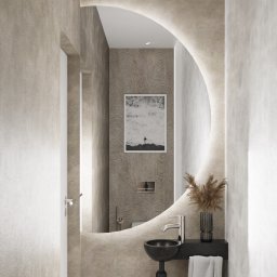 Cognac Architects - Minimalistyczna łazienka z owalnym lustrem podświetlanym LED, czarną umywalką nablatową i beżowymi ścianami o fakturze betonu. W lustrze odbija się grafika z motywem oceanu.