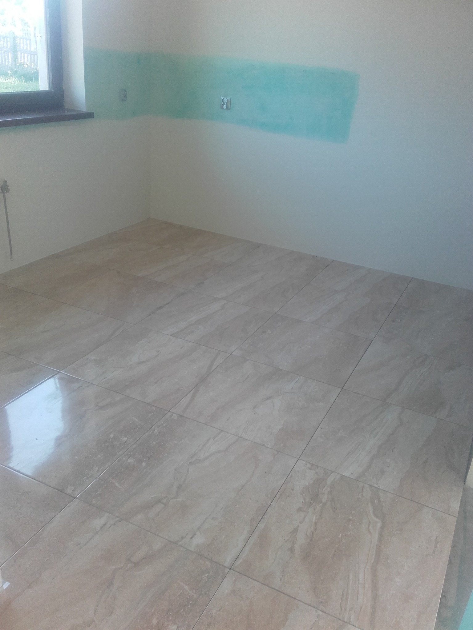 Wyłożona beżowymi płytkami podłoga w pomieszczeniu z fragmentem pomalowanej na turkusowo ściany i oknem.