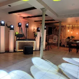 Sala bankietowa z oświetleniem eventowym, barem prosecco na kółkach, kolumnami i dekoracjami roślinnymi.