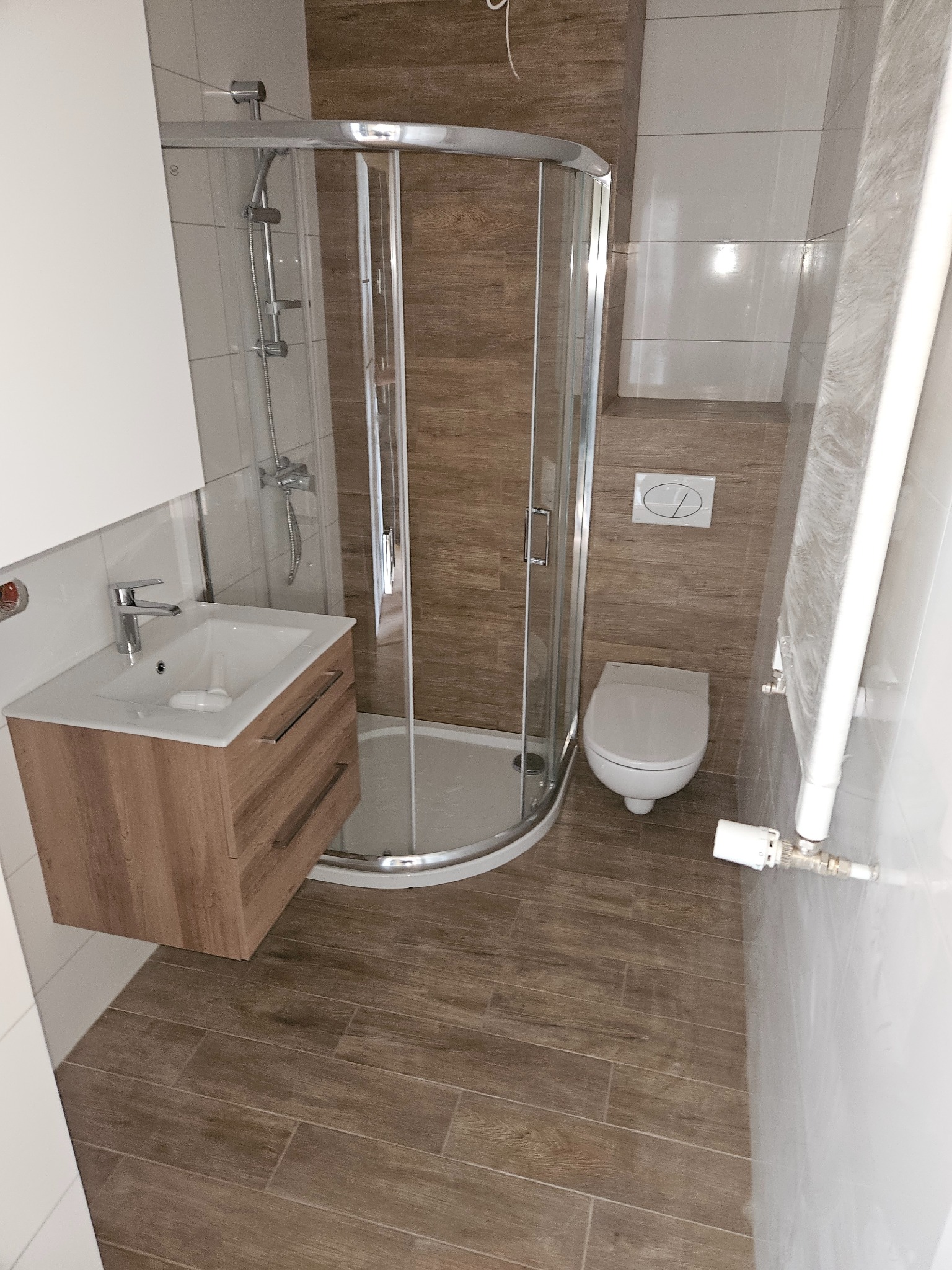 Wykończona łazienka w Żerkowie z kabiną prysznicową, umywalką z szafką w kolorze drewna i toaletą. Podłoga i ściany wyłożone płytkami imitującymi drewno.