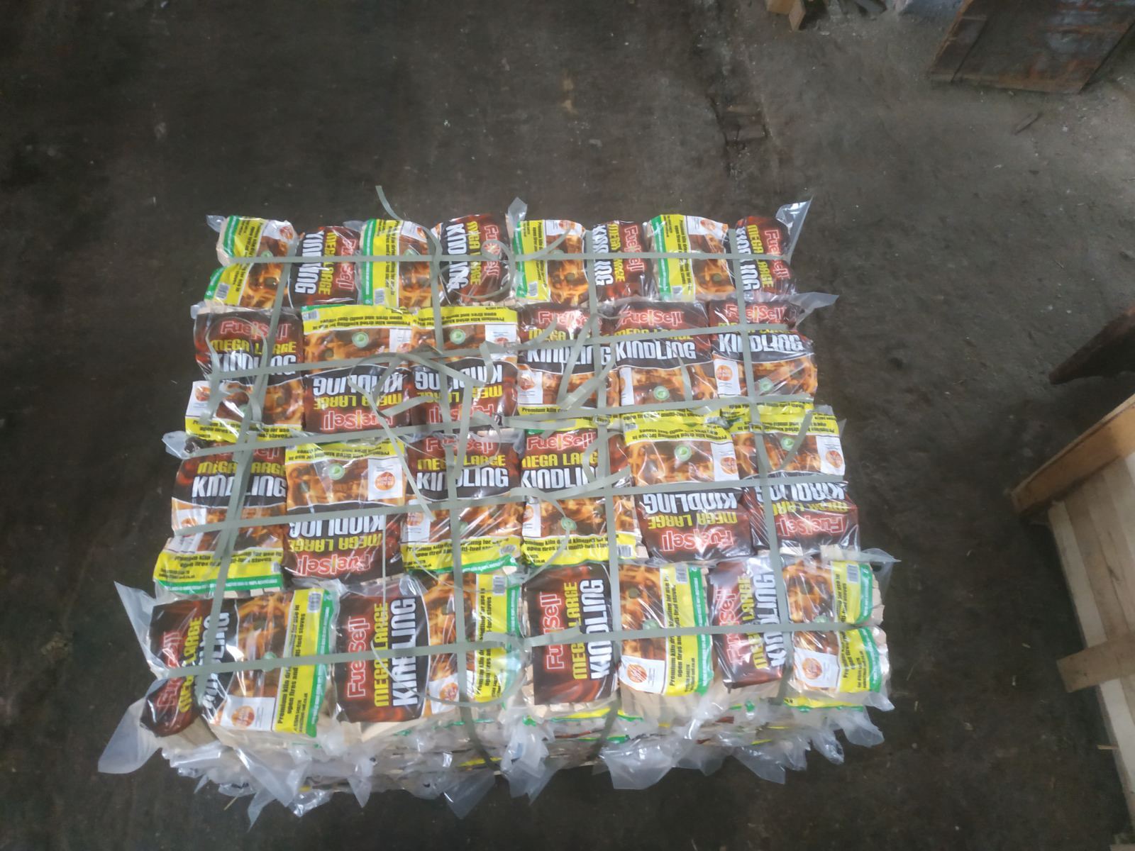 Paczki rozpałki kominkowej 'Fuel Sell Mega Large Kindling' spięte sznurkiem na betonowej podłodze magazynu.