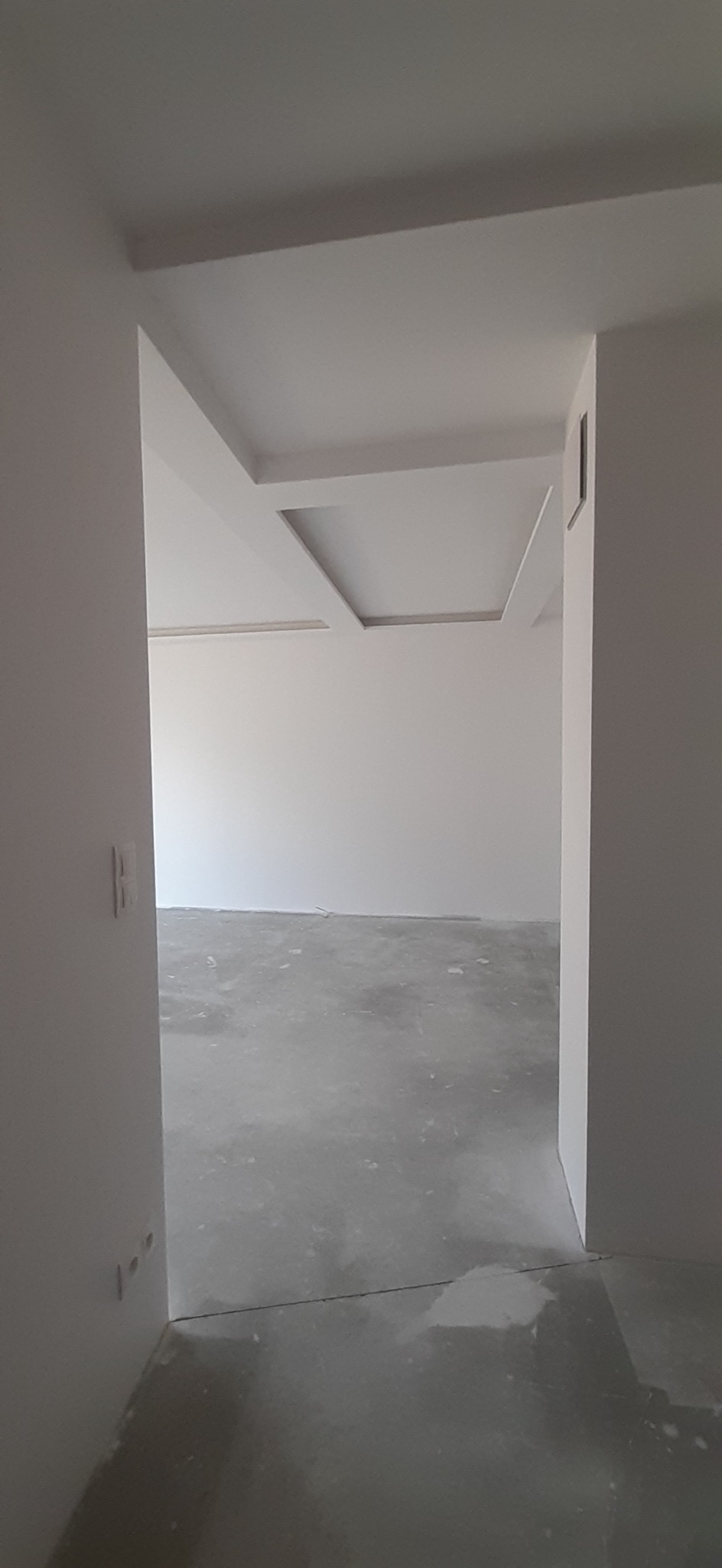 Widok z korytarza na świeżo pomalowane, puste pomieszczenie z dekoracyjnym podwieszanym sufitem. Podłoga w trakcie wykańczania, widoczne ślady po pracach remontowych.