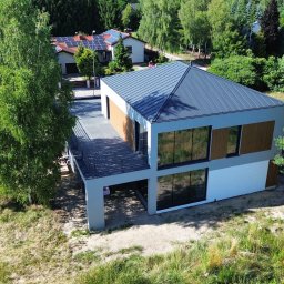 Paweł Mejza BUDOWNICTWO - Nowoczesny, dwukondygnacyjny dom z płaskim dachem i dużymi oknami, widziany z lotu ptaka, otoczony zielenią. Minimalistyczna architektura z elementami drewna.