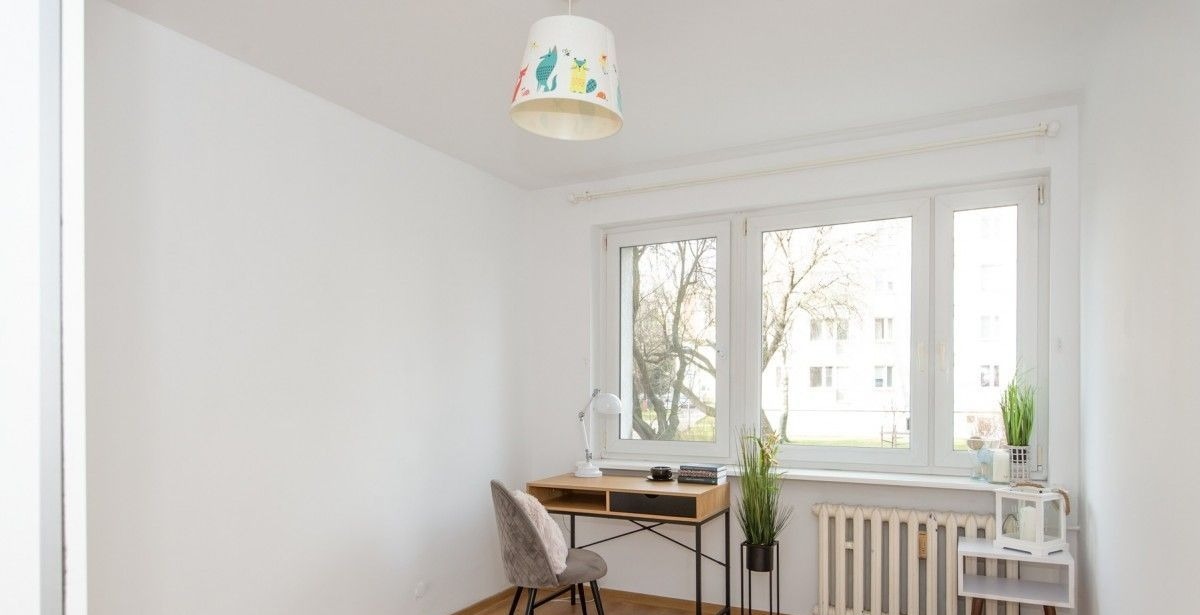 Pomalowany na biało pokój z biurkiem, krzesłem i lampą z motywem zwierzęcym, widok na drzewa za oknem.