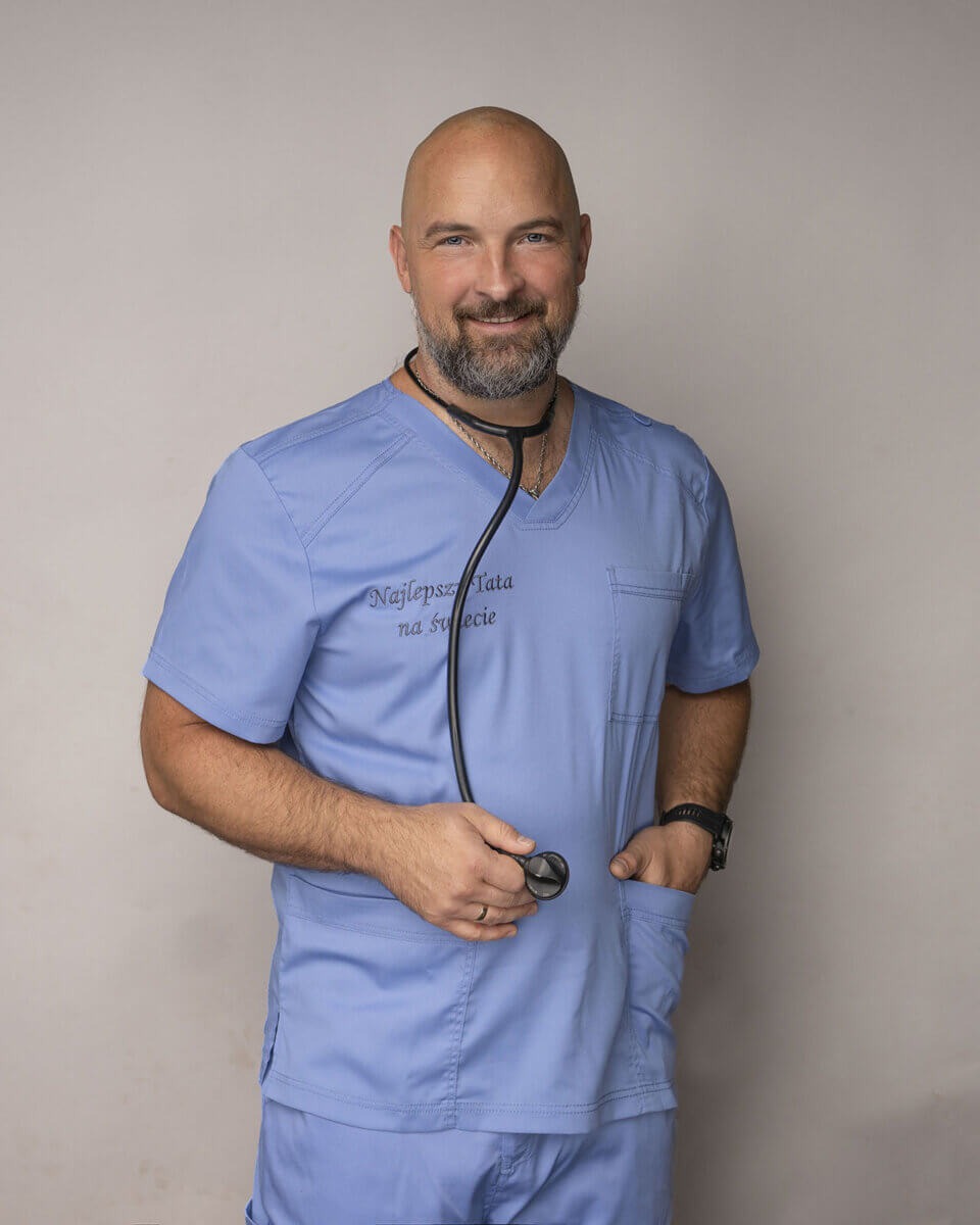 Uśmiechnięty lekarz w niebieskim uniformie z napisem 'Najlepszy Tata na świecie' i stetoskopem, zegarek na lewym nadgarstku, obrączka na palcu.