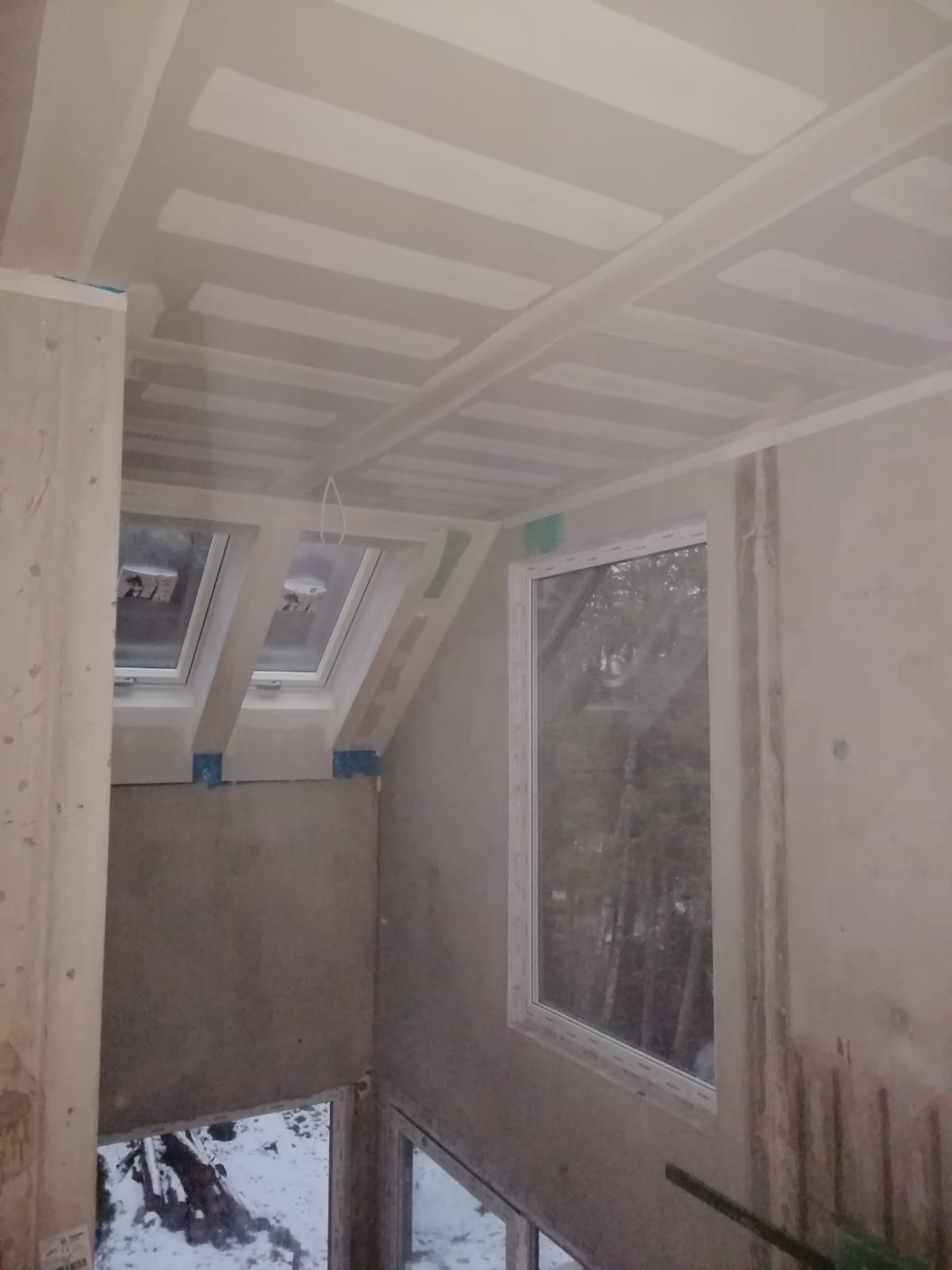 Poddasze w trakcie wykańczania: widoczne płyty na suficie i skośnych ścianach, przygotowane do dalszych prac wykończeniowych, okna dachowe i standardowe okno PCV.