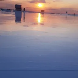 Biała, płaska powierzchnia dachu odbijająca zachodzące słońce, widoczne kominki wentylacyjne i przewody elektryczne.