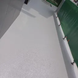 Świeżo wylana, gładka, szara powierzchnia posadzki przy wejściu do budynku, zabezpieczona barierą ochronną z zieloną plandeką.