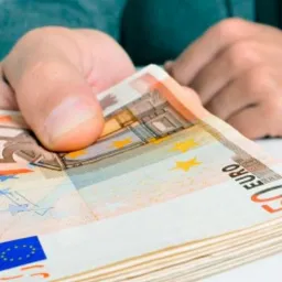 Dłoń podaje plik banknotów 50 euro na białym tle, widoczne detale zabezpieczeń i nominał.