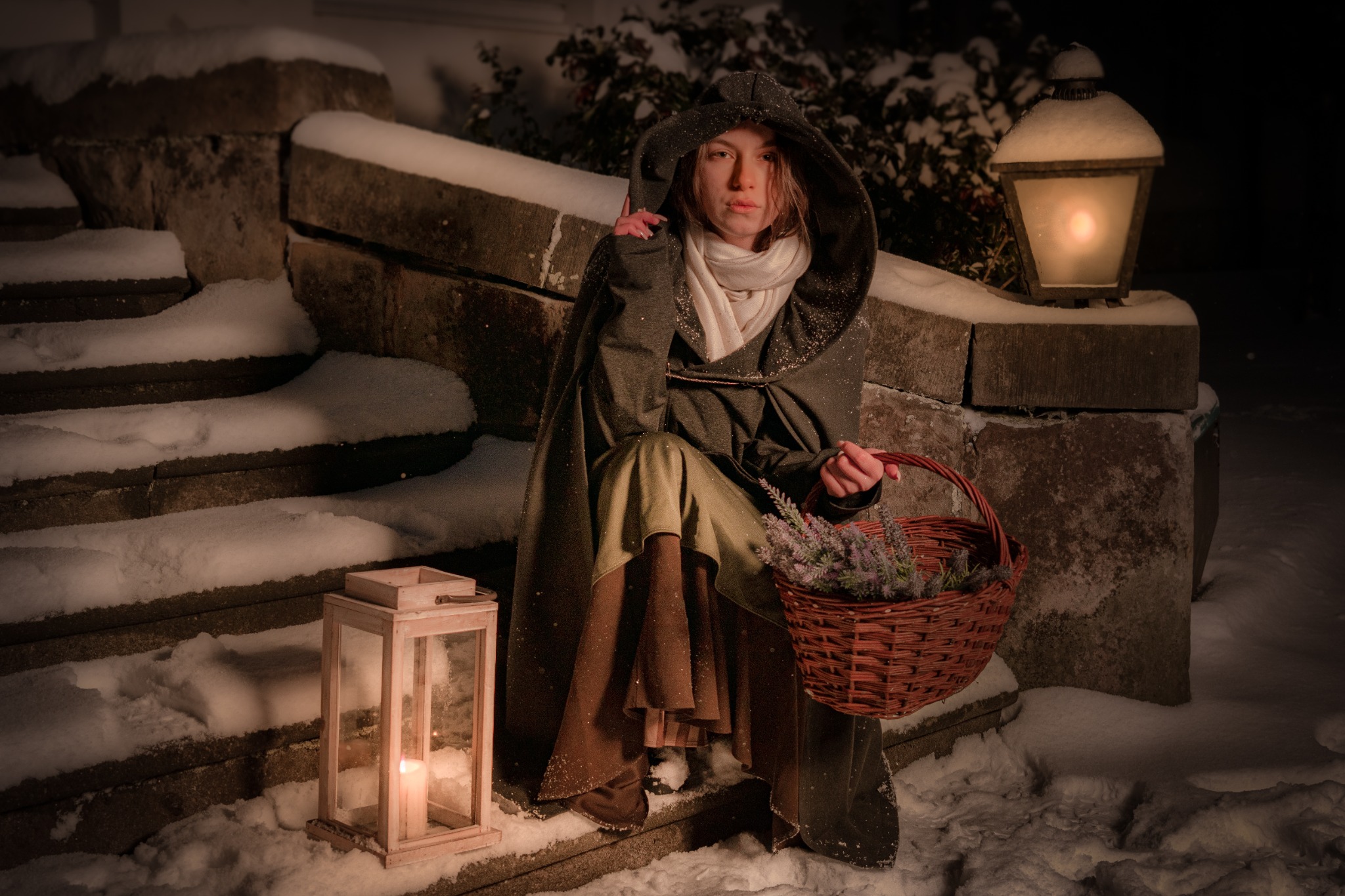 Kobieta w płaszczu z kapturem siedzi na ośnieżonych schodach z koszykiem lawendy, oświetlona ciepłym światłem latarni.