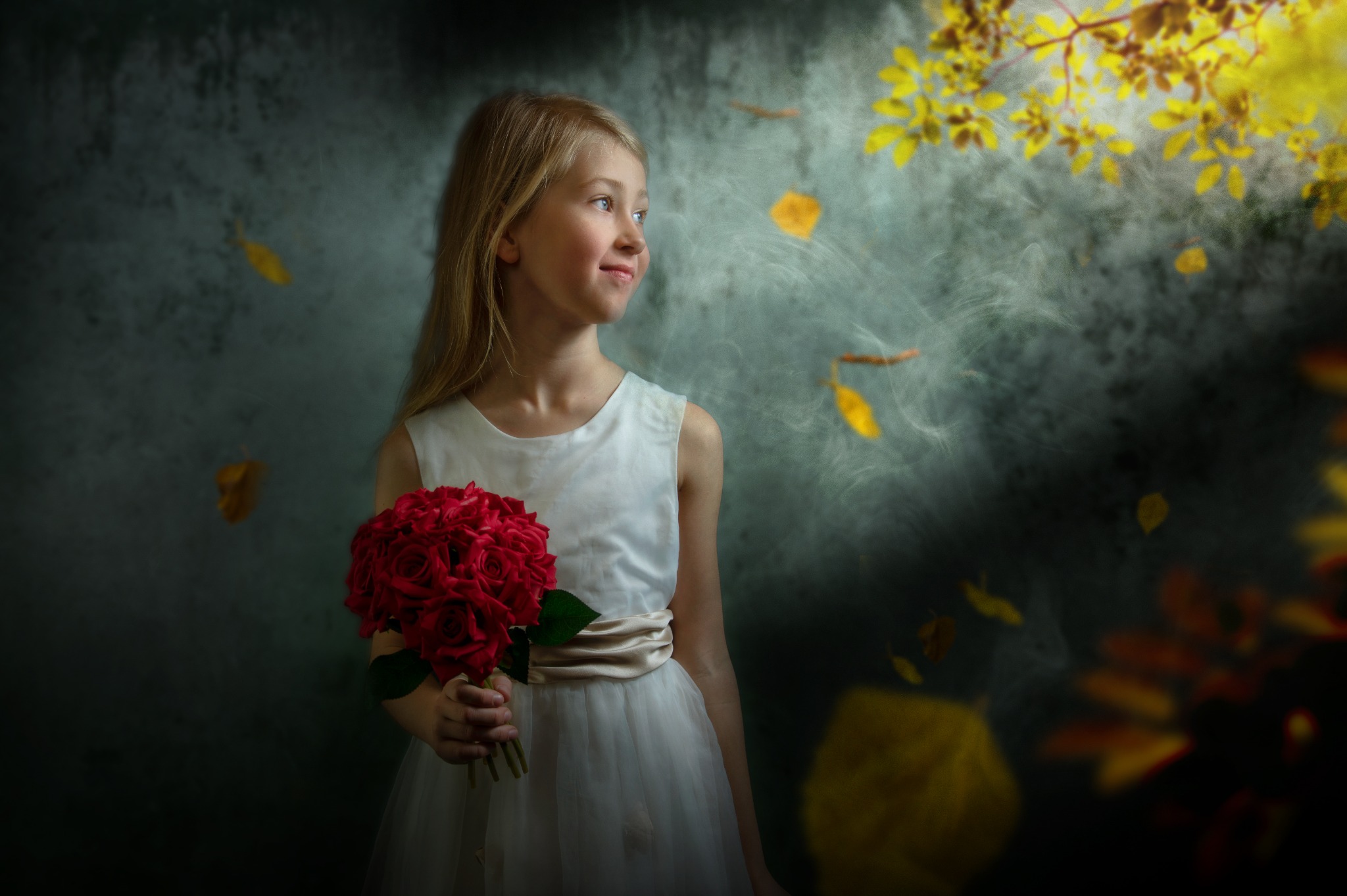 Dziewczynka w białej sukience z bukietem czerwonych róż, spoglądająca w prawo, z jesiennymi liśćmi opadającymi w tle na rozmytym, ciemnym tle.