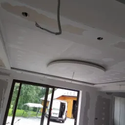 Sufit podwieszany z płyt kartonowo-gipsowych w trakcie montażu, widoczne łączenia wymagające szpachlowania, okrągły element dekoracyjny, instalacja elektryczna wyprowadzona na zewnątrz.