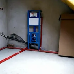 Surowy stan łazienki na poddaszu z częściowo rozprowadzoną instalacją hydrauliczną w kolorze czerwonym, widoczny stelaż podtynkowy WC w kolorze niebieskim, oraz przygotowane podejścia kanalizacyjne.