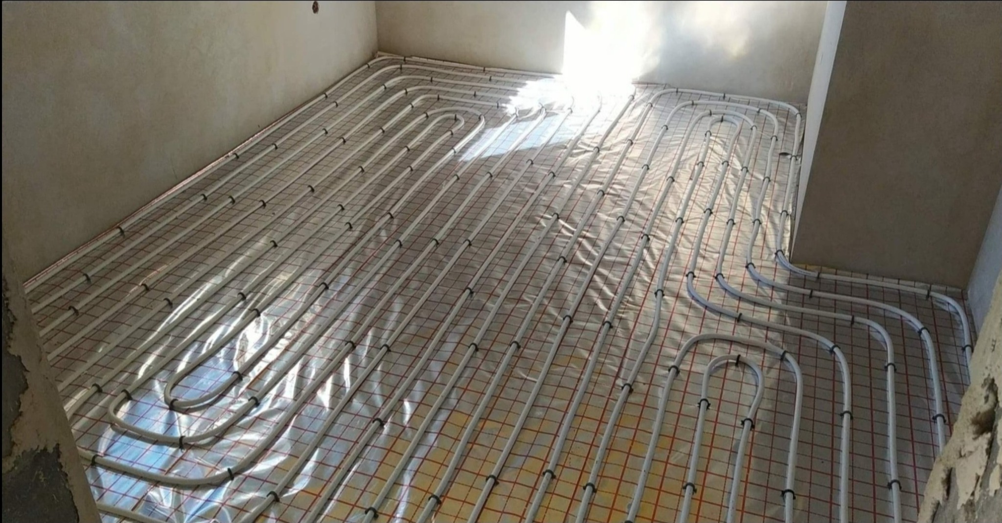 Układanie rur ogrzewania podłogowego na folii refleksyjnej z siatką w Żywcu, widoczne mocowania i surowe ściany w tle.