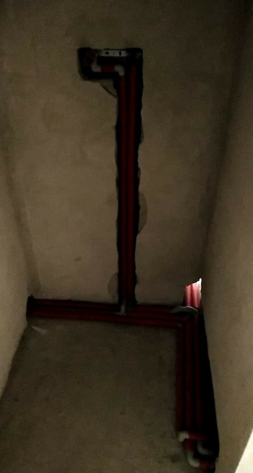 Czerwone rury instalacji wodnej w bruzdach w surowej ścianie podczas remontu, widoczne łączenia i pionowy przebieg instalacji.