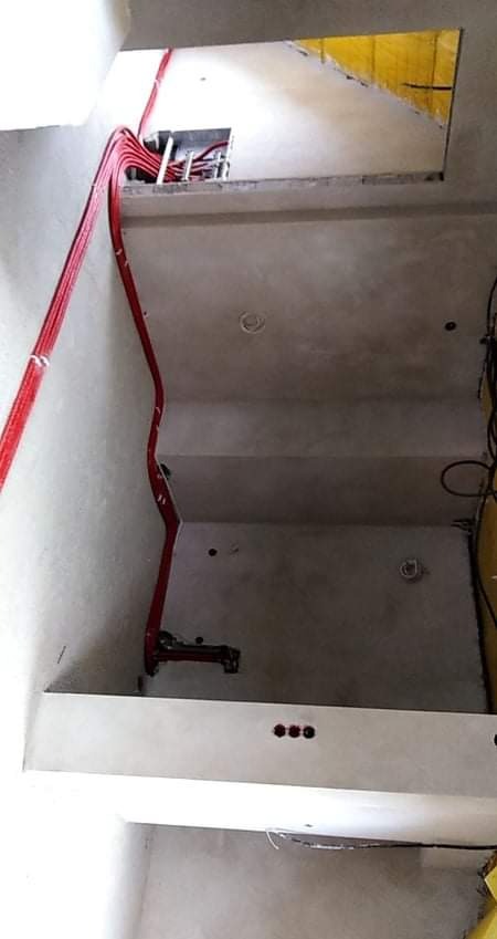 Wewnętrzne ściany w surowym stanie z widocznymi czerwonymi przewodami instalacji poprowadzonymi wzdłuż nich, otwór w ścianie z widoczną izolacją.