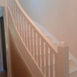 D.S.COLOR - Biała, kręta klatka schodowa z drewnianą balustradą po odświeżeniu, widoczna ściana w jasnym odcieniu i fragment sufitu z ozdobnym żyrandolem.