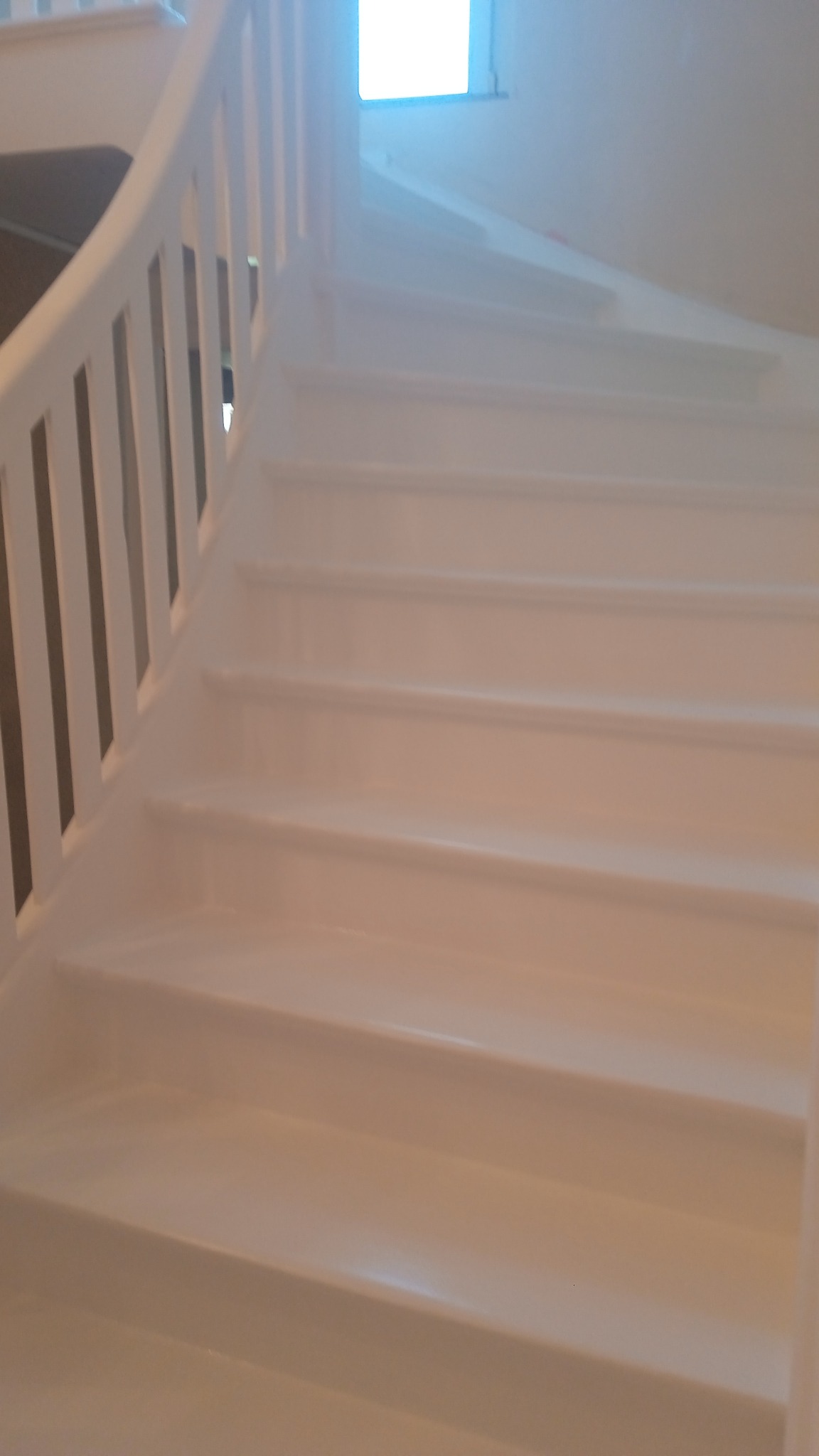 Białe, spiralne schody z drewnianą balustradą, świeżo po malowaniu, widok z dołu, z oknem w tle.