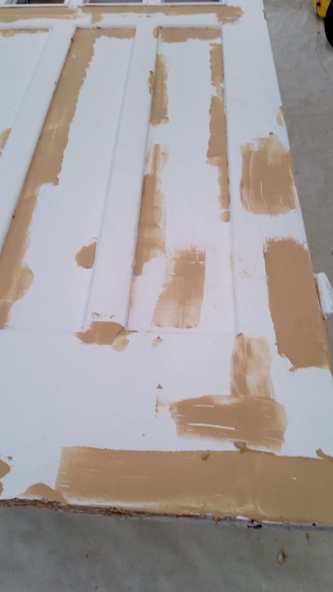 Białe, panelowe drzwi w trakcie malowania, z widocznymi śladami brązowego podkładu na powierzchni i krawędziach.