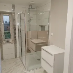 Nowoczesna łazienka z kabiną prysznicową typu walk-in, białą szafką pod umywalką i marmurową podłogą, akcenty srebrnej mozaiki przy oknie.