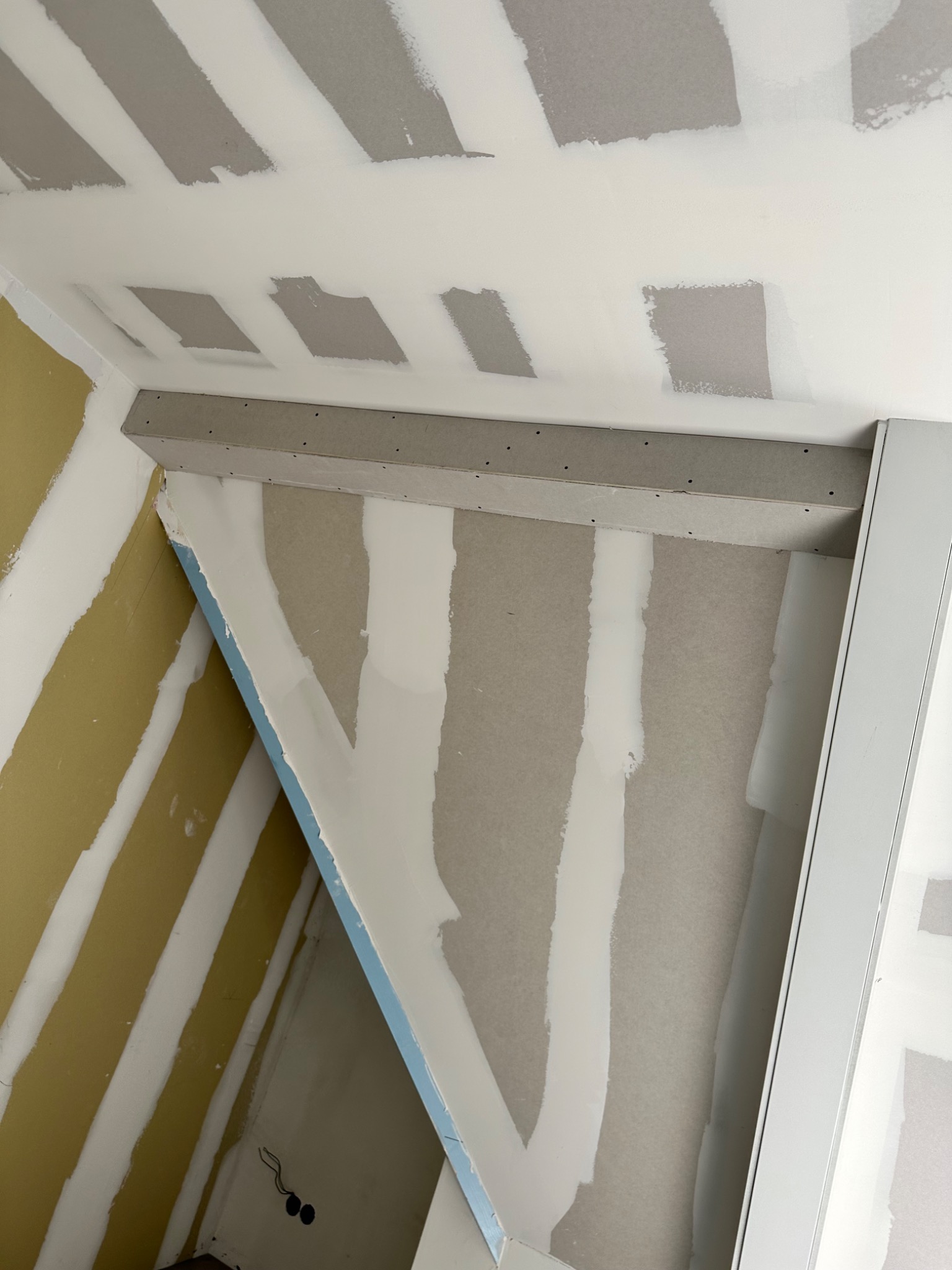 Wnętrze w trakcie prac wykończeniowych: ściany z płyt kartonowo-gipsowych z widocznymi łączeniami szpachlowanymi, częściowo pomalowane, widoczna konstrukcja sufitu podwieszanego z profilami...