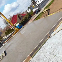 Świeżo wylany fundament pod budynek jednorodzinny, widoczna pompa do betonu, drewniane szalunki i zbrojenie.