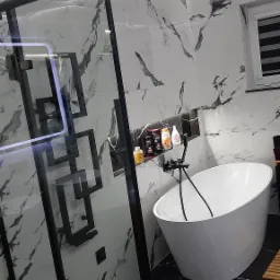 Nowoczesna łazienka w Łukowicy z białą wanną wolnostojącą, czarną armaturą i kabiną prysznicową z geometrycznymi zdobieniami, wykończona marmurowymi płytkami.