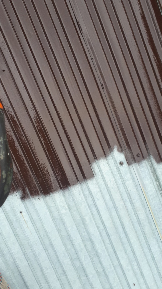 Częściowo pomalowany blaszany dach w kolorze brązowym, widoczne ślady farby i surowa blacha.