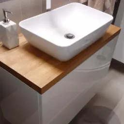 Biała, prostokątna umywalka nablatowa z drewnianym blatem i białą szafką pod umywalkę, nowoczesna bateria chromowana, dozownik mydła o geometrycznym kształcie