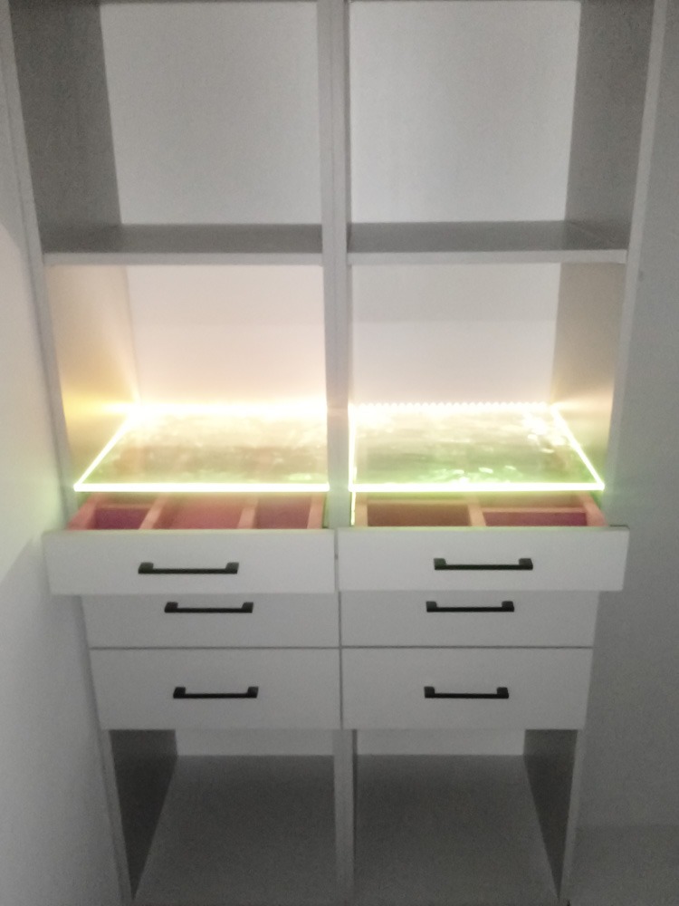 Biała szafa wnękowa z podświetlanymi półkami i szufladami z czarnymi uchwytami, widok z bliska na dolną część szafy.