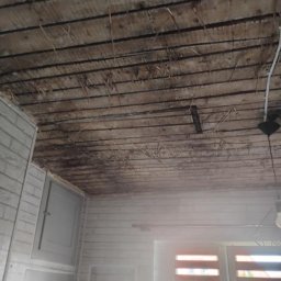 Rafał Niewęgłowski - Drewniany sufit z widocznymi belkami i fragmentami izolacji, ściany wyłożone białą cegłą, okno z żaluzjami. Widok na wnętrze w trakcie prac remontowych.