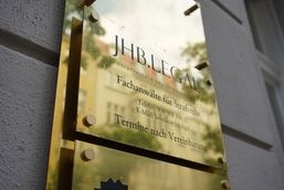 Złota tabliczka informacyjna z napisem 'JHB.LEGAL Fachanwälte für Strafrecht' przy wejściu do biura w Berlinie, widoczna z boku, z refleksami światła.