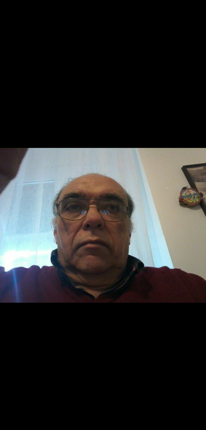 Portret mężczyzny w okularach, z poważnym wyrazem twarzy, w pomieszczeniu z jasnymi ścianami i dekoracją.