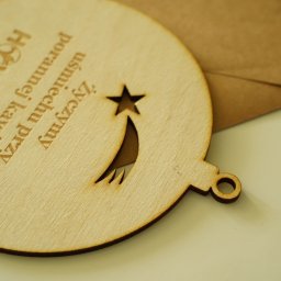 Form-Art Pracowania Atystyczna - Drewniana zawieszka w kształcie bombki z wygrawerowanym tekstem 'Życzymy uśmiechu przy porannej kawie...' i logiem firmy 'HOWLITA', na tle koperty.