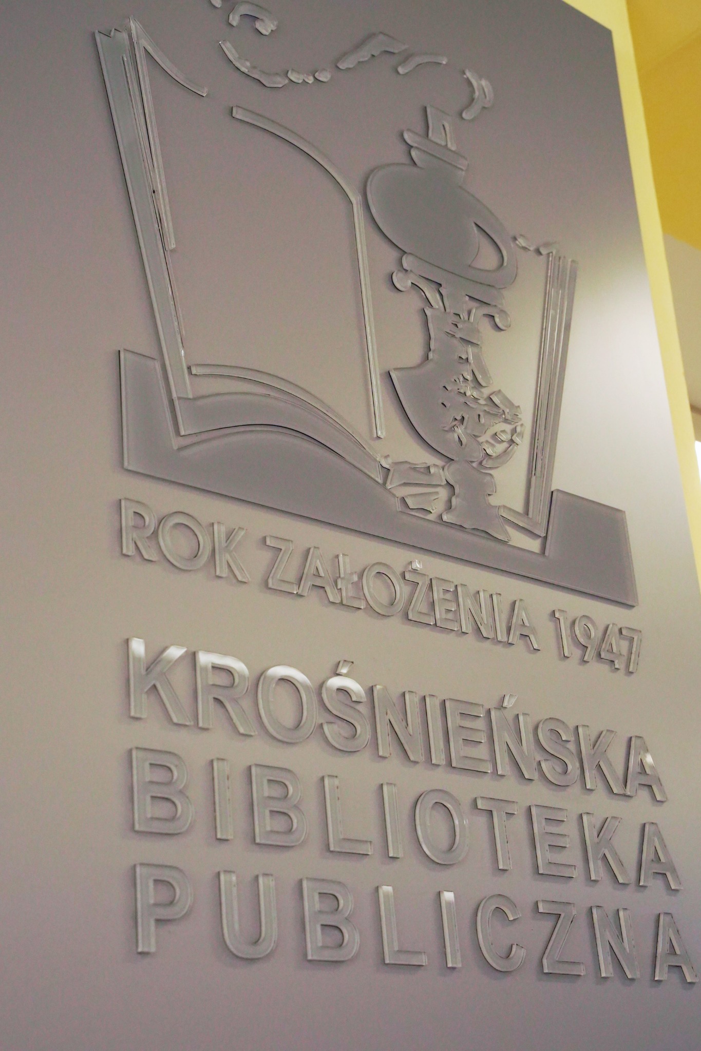 Ściana z transparentnego akrylu, na której umieszczono logo i nazwę 'Krośnieńska Biblioteka Publiczna' oraz rok założenia 1947, podświetlona z góry.