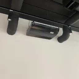 Czarna klimatyzacja kasetonowa zamontowana pod czarnym sufitem z widocznymi rurami wentylacyjnymi i oświetleniem punktowym.