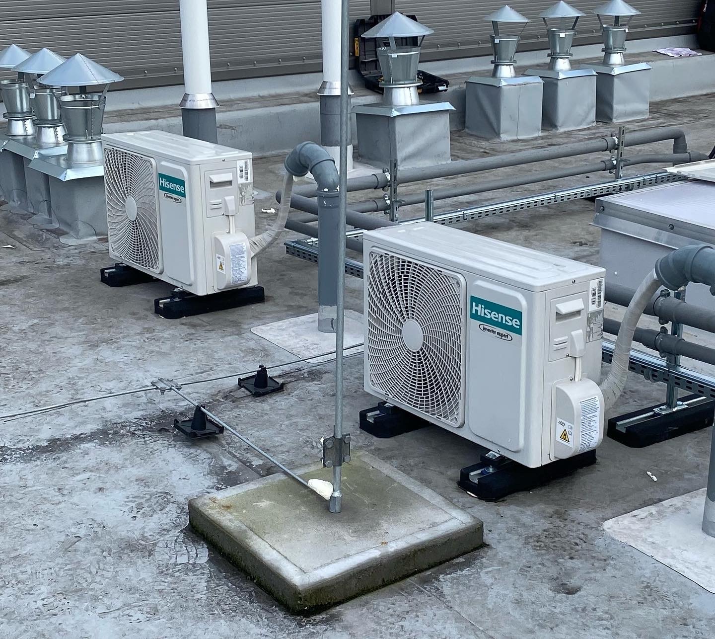 Instalacja klimatyzatorów Hisense na dachu budynku, widoczne elementy montażowe, rury i kominki wentylacyjne.