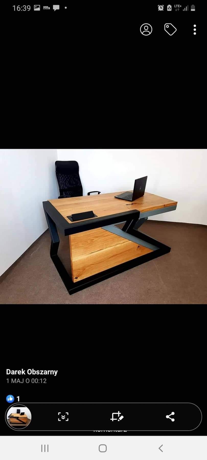 Nowoczesne biurko z blatem z jasnego drewna i czarną metalową podstawą o geometrycznym kształcie, uzupełnione czarnym krzesłem biurowym i laptopem.