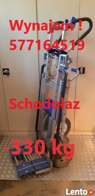 Schodołaz transportowy, srebrna konstrukcja z niebieskimi elementami na kółkach, widoczne naklejki z informacjami o wynajmie i wadze maksymalnej, stoi na metalowej podłodze.