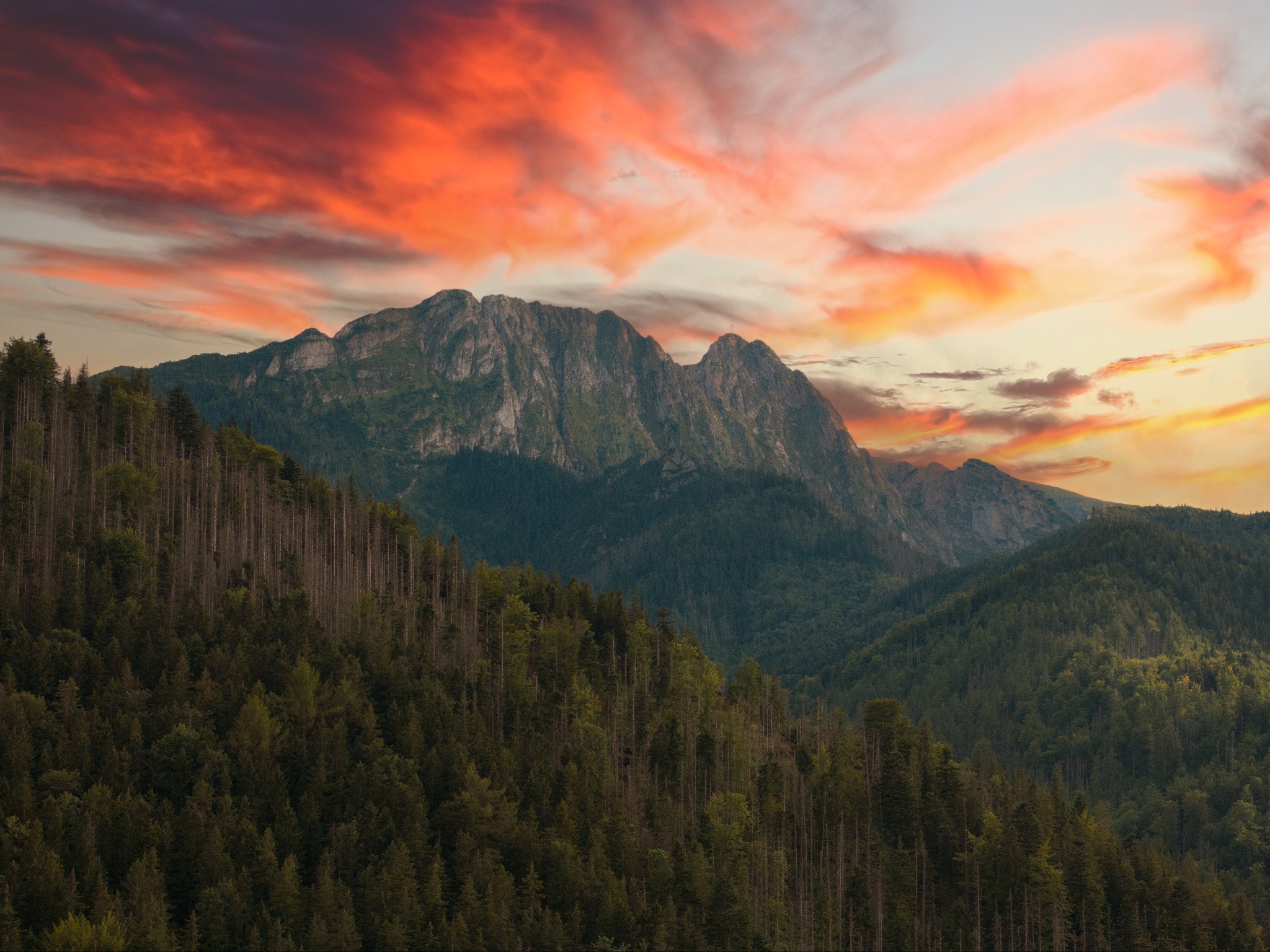 Panorama górskich szczytów porośniętych lasem iglastym, malownicze, pomarańczowo-czerwone chmury o zachodzie słońca.