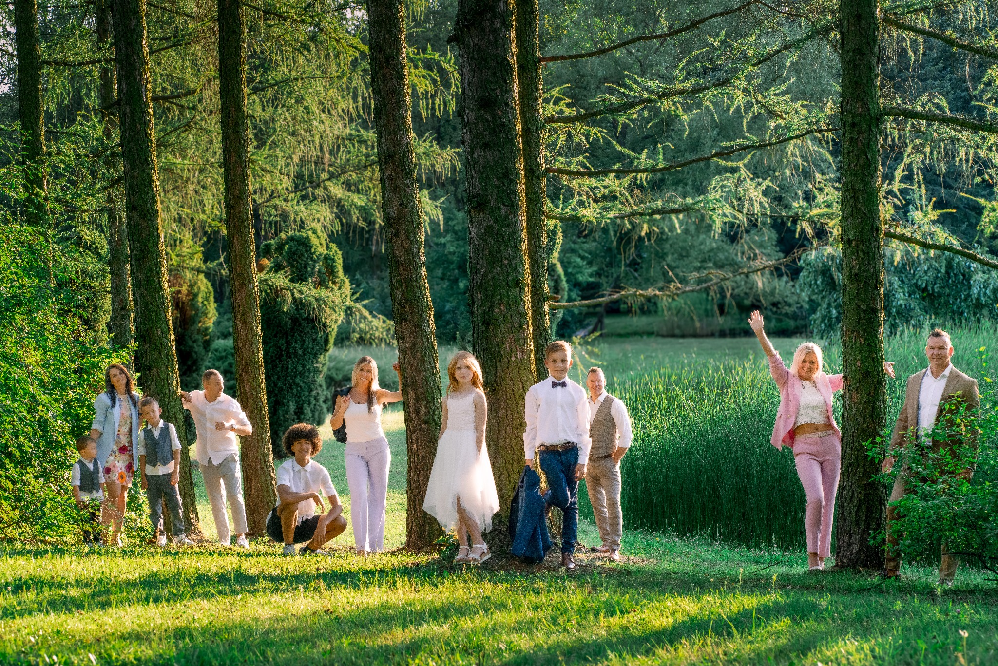 Duża, wielopokoleniowa rodzina pozuje w lesie, ubrana w eleganckie stroje na sesji zdjęciowej, z delikatnym światłem słonecznym przebijającym przez drzewa.