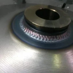 Metalowy element połączony spoiną z widocznymi śladami obróbki, z bliska.