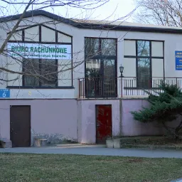 Budynek biura rachunkowego z zielonym banerem informacyjnym nad wejściem, widoczny numer budynku '6'.