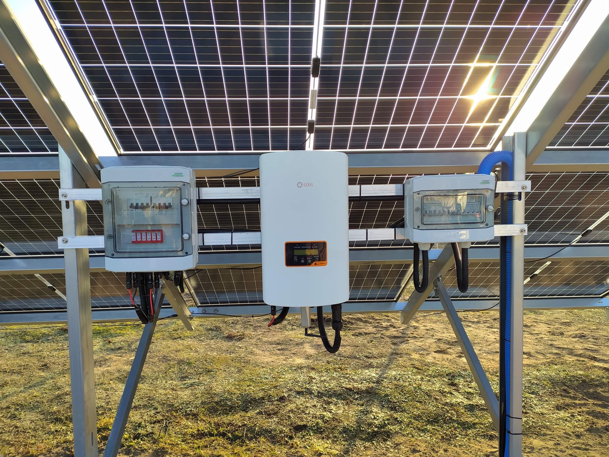 Panel słoneczny z widocznym inwerterem Solis i skrzynkami zabezpieczeń DC, zamontowany na metalowej konstrukcji na zewnątrz.