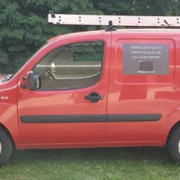 Czerwony samochód dostawczy z naklejkami reklamowymi usług: serwis komputerowy, strony internetowe, sieci komputerowe, automatyka bram, monitoring, domofony, alarmy i numerem telefonu, drabina...