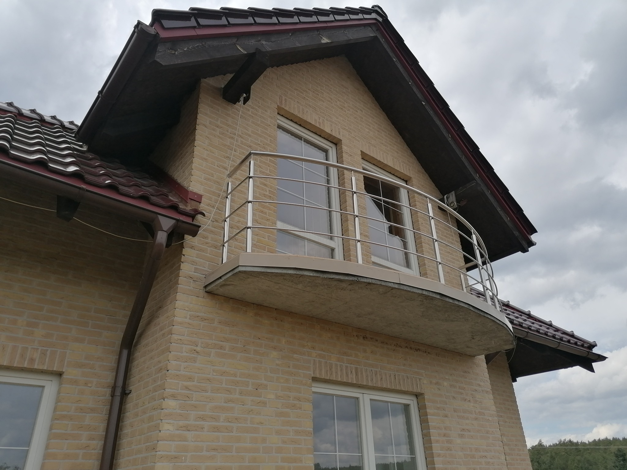 Kremowy, dwupiętrowy dom z cegły klinkierowej z balkonem zabezpieczonym metalową, półokrągłą barierką, widok z dołu.