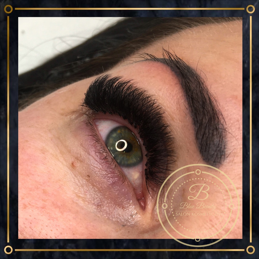 Zbliżenie na oko z przedłużonymi, gęstymi rzęsami i podkreślonym łukiem brwiowym; widoczne logo salonu kosmetycznego w rogu zdjęcia.