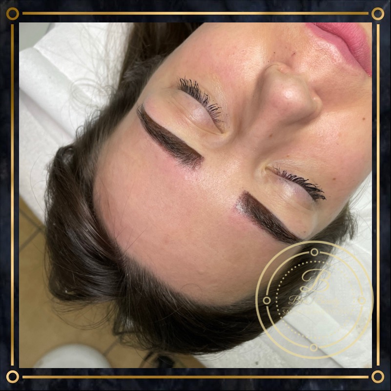 Kobieta z zamkniętymi oczami leżąca na plecach, prezentująca świeżo wykonany permanentny makijaż brwi metodą pudrową, z widocznym logo salonu w rogu.